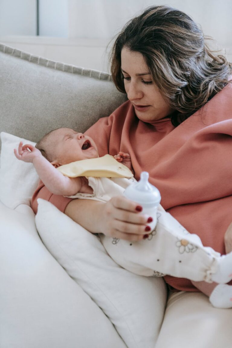 Young mother in casual clothes hugging and trying to calm crying baby before feeding with milk from bottle