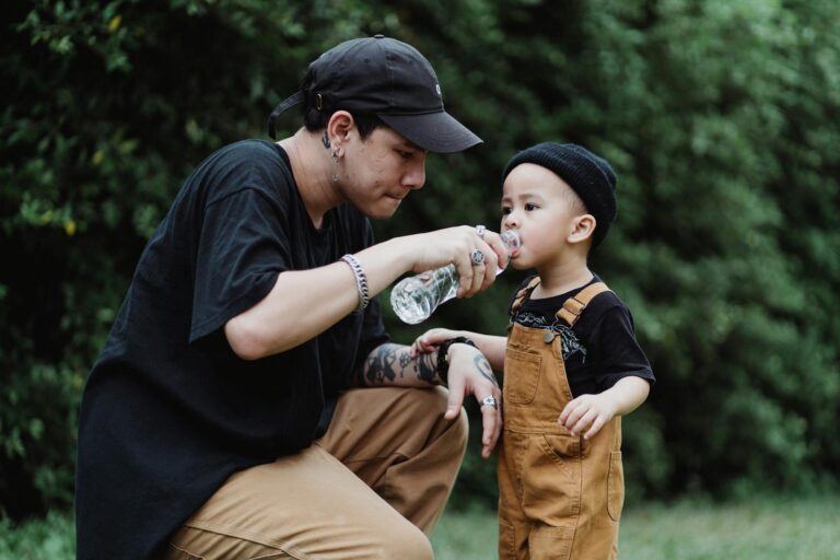 A father sharing a water bottle with his son in a lush green outdoor setting.