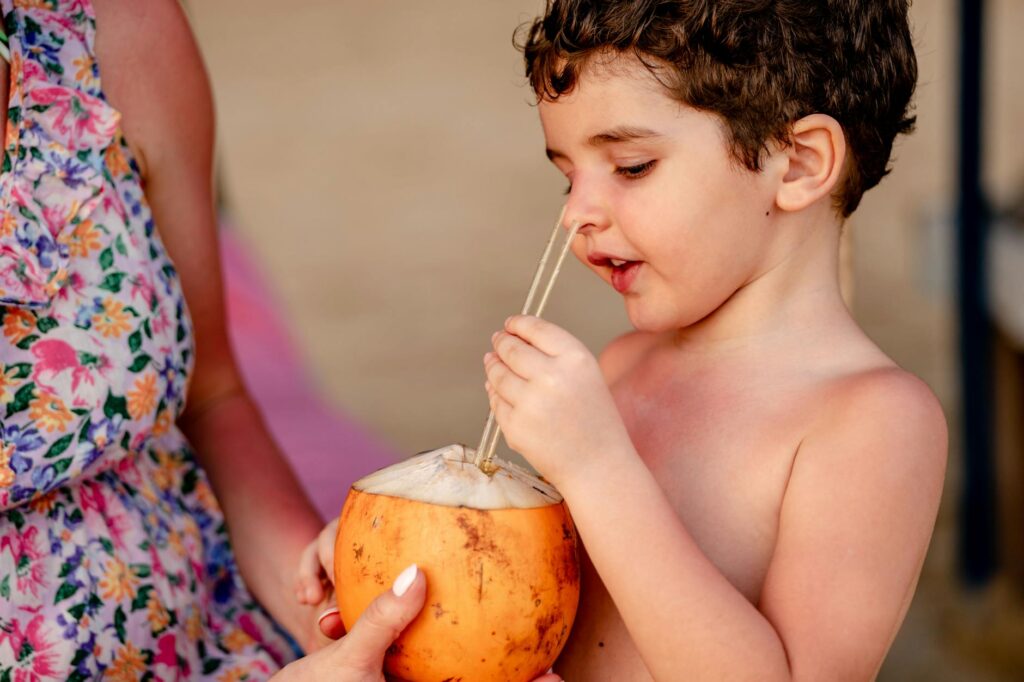 A young child drinks fresh coconut water outdoors with a straw, embracing a tropical vibe.